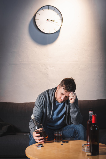 depressed man holding bottle of whiskey while sitting at home alone - Foto, Bild