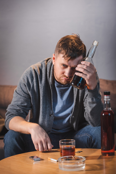 drunk, alcohol-addicted man holding bottle of whiskey at home - Foto, Bild