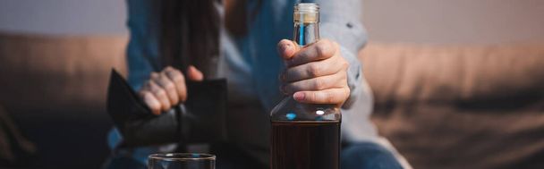vista recortada de la mujer alcohólica sosteniendo botella y cartera vacía sobre fondo borroso, pancarta - Foto, Imagen