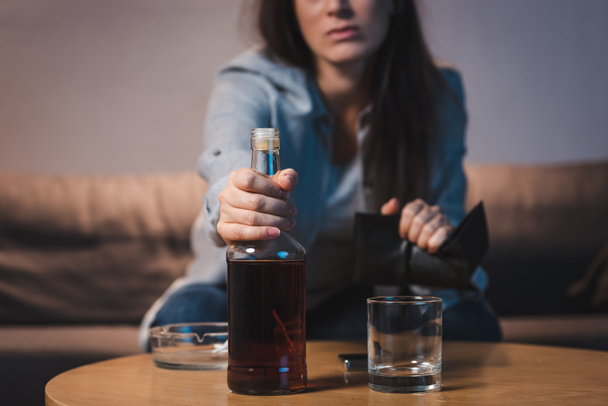 vista recortada de la mujer adicta tomando botella de whisky de la mesa, fondo borroso - Foto, Imagen