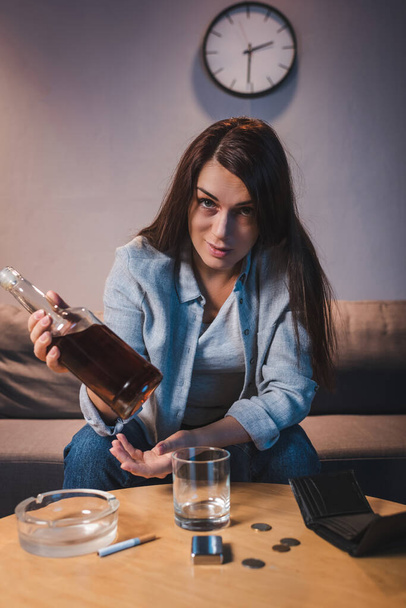 uzależniona od alkoholu kobieta patrząca w kamerę trzymając butelkę whisky   - Zdjęcie, obraz