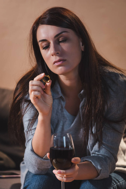 drunk woman holding wedding ring and glass of red wine while sitting at home alone    - Фото, зображення