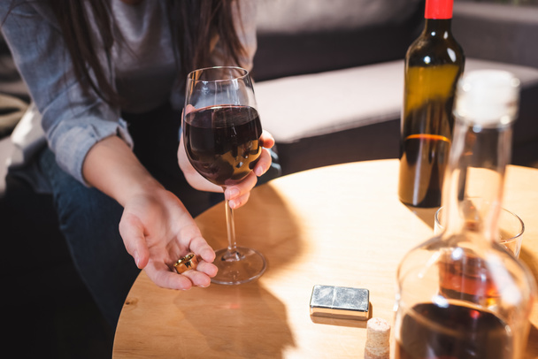 cropped view of alcoholic woman holding wedding rings and glass of wine near bottles on blurred foreground     - Foto, afbeelding