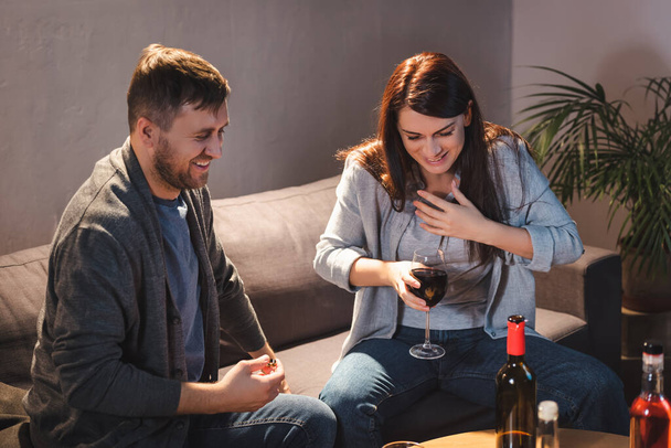 excited, drunk woman holding glass of red wine while sitting near husband  - Foto, Bild