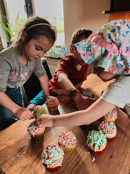 Group of children baking cupcakes, preparing ingredients, topping, sprinkles for decorating cookies. Kids cooking, working together in kitchen at home. Concept of happy family - Fotó, kép