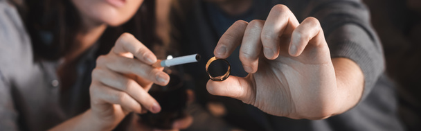 cropped view of alcohol-addicted husband and wife holding wedding ring and cigarette, blurred background, banner - Foto, afbeelding