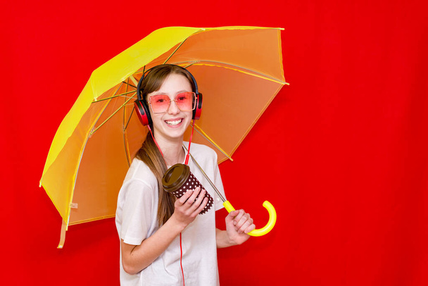 Teini-ikäinen tyttö kuuntelee musiikkia kuulokkeissa, joissa on sateenvarjo. punainen studio tausta yllään valkoinen t paita. Studio shot. - Valokuva, kuva