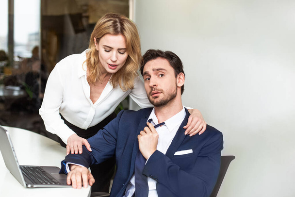 Seducing a subordinate in office. Caucasian blonde woman touching male colleague, who sits at table looking at camera looking bewildered. Copy space at right side - Valokuva, kuva