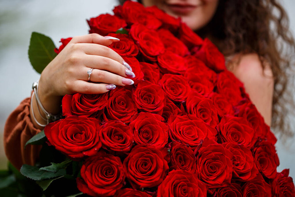 Hand of a girl with a wedding ring close-up on a bouquet of red roses - Foto, afbeelding