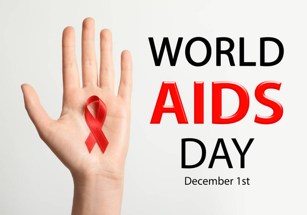 World AIDS Day poster. Woman holding in hand red awareness ribbon near text on light background, closeup - Foto, immagini