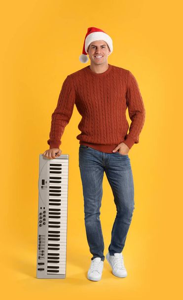 Man in Santa hat with synthesizer on yellow background. Christmas music - Фото, изображение