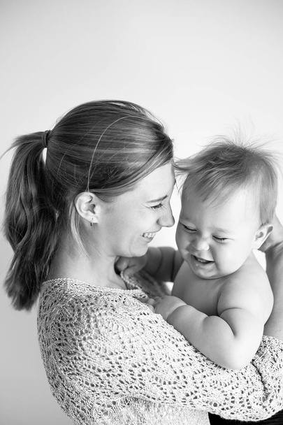 young mom laughs and hugs her son, baby 1 year old, baby care leave, happy motherhood and childhood, black and white photo, selective focus - Photo, Image