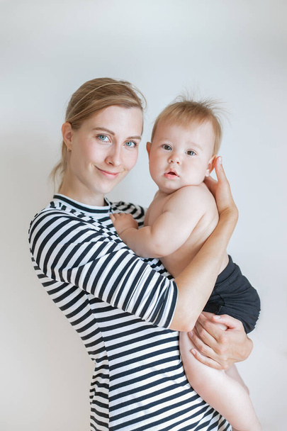 joven madre sostiene a su hijo en sus brazos, mirando a la cámara, retrato de una madre con un bebé de 1 año - Foto, imagen