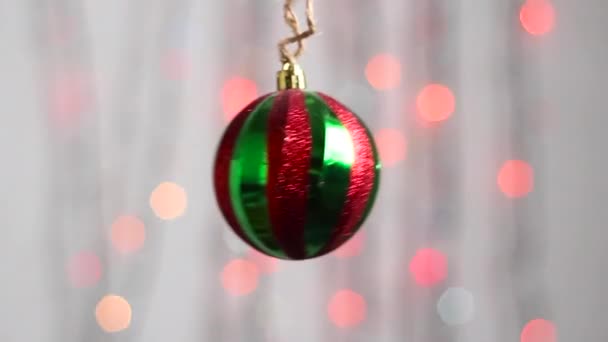 Hermoso juguete árbol de Navidad cuelga en el fondo de las luces multicolores de Año Nuevo. Primer plano. Juguete árbol de Navidad en forma de una esfera rojo-verde. - Imágenes, Vídeo