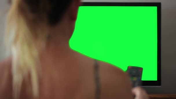 Žena se dívá na televizi se zelenou obrazovkou. Zelenou obrazovku můžete nahradit záběrem nebo obrázkem, který chcete. Můžete to udělat s klíčovým efektem v After Effects nebo s jiným softwarem pro editaci videa (podívejte se na návody na YouTube).   - Záběry, video