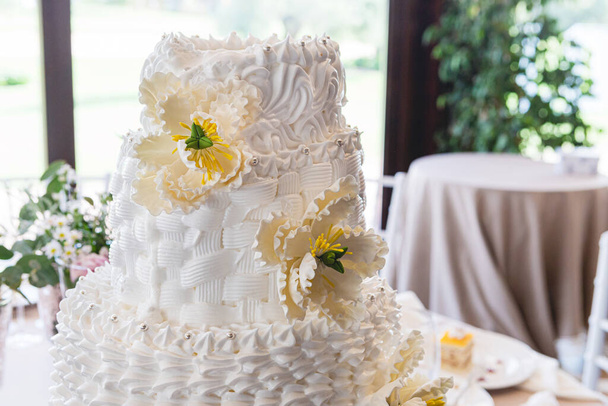 Detail einer wunderschönen Hochzeitstorte mit Fondant-Blumen auf einem Hochzeitstisch - Foto, Bild
