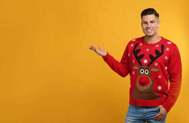 Handsome man in Christmas sweater on yellow background, space for text - Foto, afbeelding