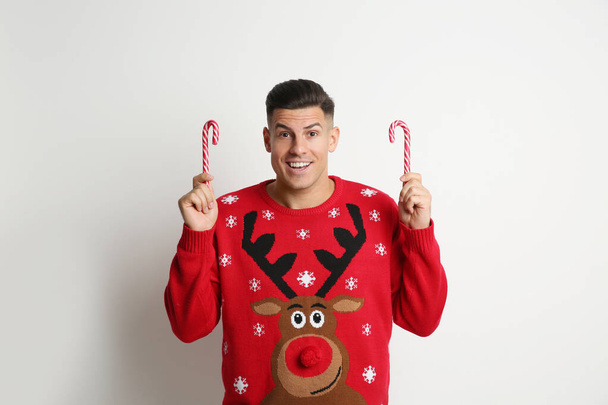 Happy man in Christmas sweater with candy canes on white background - Фото, изображение