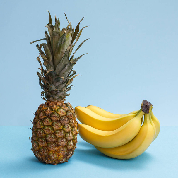 Naturalny skład z owoców tropikalnych. Świeże ananasy i banany na niebieskim tle. - Zdjęcie, obraz