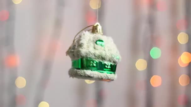 Bonito brinquedo de árvore de Natal pendura no fundo de luzes de Natal multi-coloridas e se move ligeiramente. Close-up. Brinquedo de árvore de Natal na forma de uma casa verde. - Filmagem, Vídeo