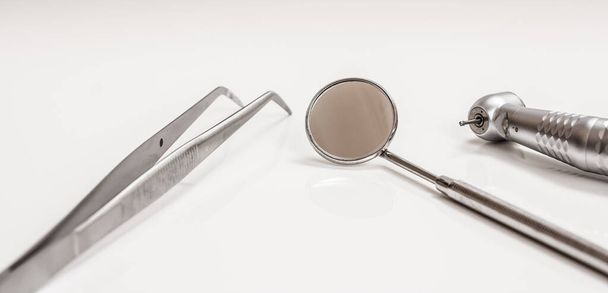 High-speed dental handpiece, a metal mirror and a tweezers. Dental instruments for dental treatment on black background. Medical tools. Close-up view. Shallow depth of field. - Photo, Image