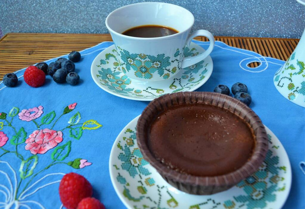 Felülnézet egy porcelán készlet kávé, egy csokoládé hűtő egy kék virág hímzett asztalterítő körül áfonya és málna - Fotó, kép
