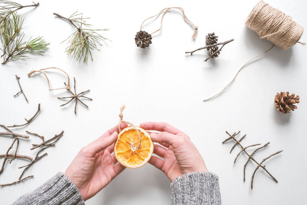 Kézzel, hogy egy házi készítésű karácsonyfa játék természetes környezetbarát anyagok szárított narancs. Top view, flat lay, szelektív fókusz. - Fotó, kép
