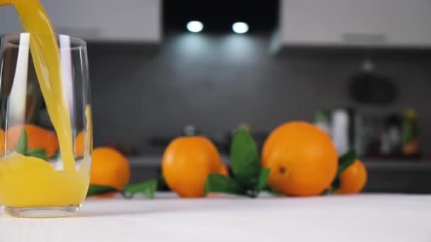 Succo d'arancia versando in vetro su tavolo bianco in cucina moderna - Filmati, video