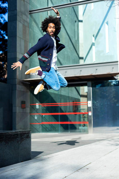 Portrait of a handsome afro black man jumping while looking camera smiling outdoors in a sunny day - Фото, изображение