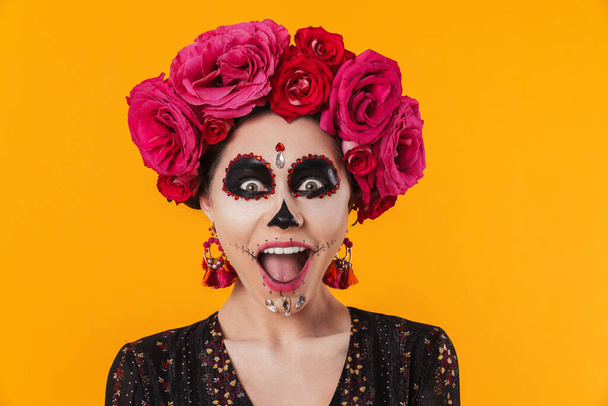 Excited girl in halloween makeup and flower wreath posing at camera isolated over yellow wall - Foto, afbeelding