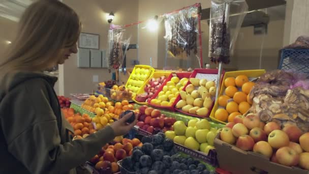 Mujer joven elige ciruelas en los estantes de la tienda en el mercado - Imágenes, Vídeo