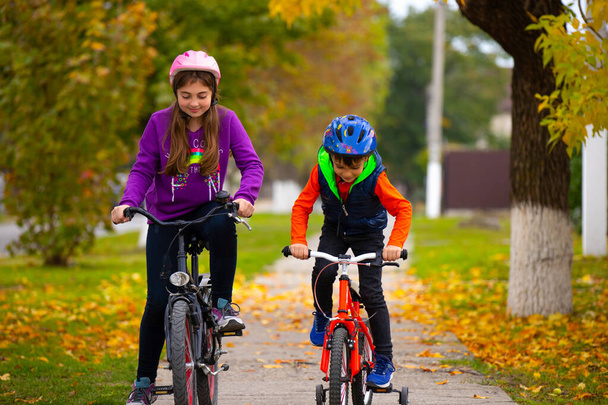 Children in helmets ride bicycles in the park. Outdoor recreation. Autumn Park. Photo with empty side space. High quality photo - Photo, Image