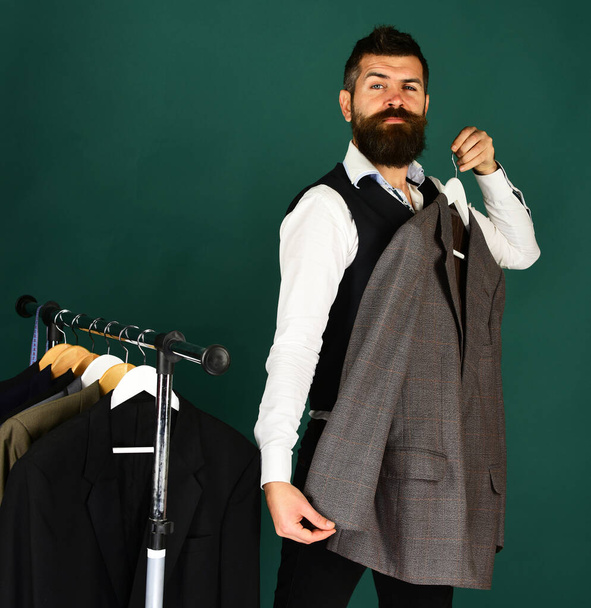 Businessman with tricky face tries jacket on green background. - Foto, Bild