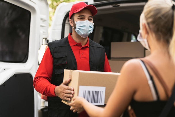 Corona virüsünün yayılmasını önlemek için maske takan teslimatçı genç bir kadın Kurye Express 'ten online sipariş paketi alıyor. - Fotoğraf, Görsel