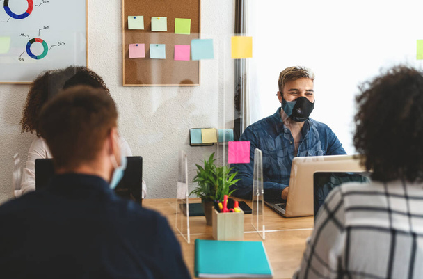 Young people in co-working creative space wearing surgical mask and keeping social distance to avoid corona virus spread - Health care and business technology concept - Photo, Image