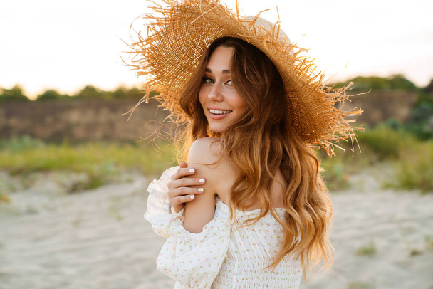Young caucasian attractive brunette woman in straw hat smiling and looking at camera outdoors - Valokuva, kuva