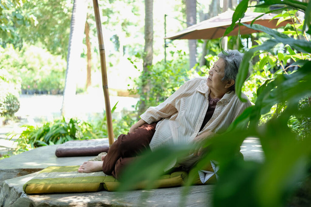 Μεγαλύτερη γυναίκα ξεκουράζεται στον κήπο. Ασιάτισσα ηλικιωμένη γυναίκα χαλαρώνει έξω. ανώτερος τρόπος ζωής αναψυχής - Φωτογραφία, εικόνα