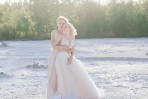 Beautiful lesbian couple walking on sand along a river bank on their wedding day - Photo, Image