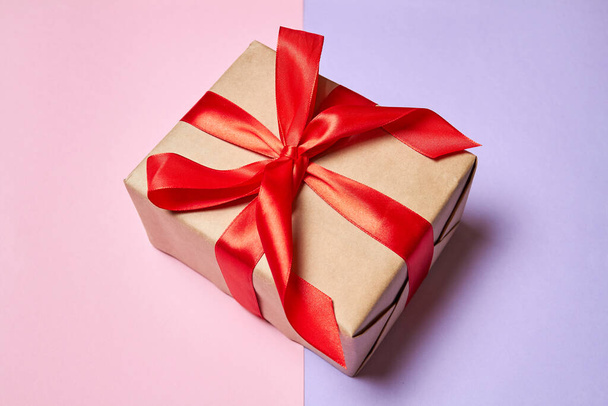 Χριστουγεννιάτικο ή Πρωτοχρονιάτικο κουτί δώρου με κόκκινη κορδέλα σε πολύχρωμο φόντο - Φωτογραφία, εικόνα