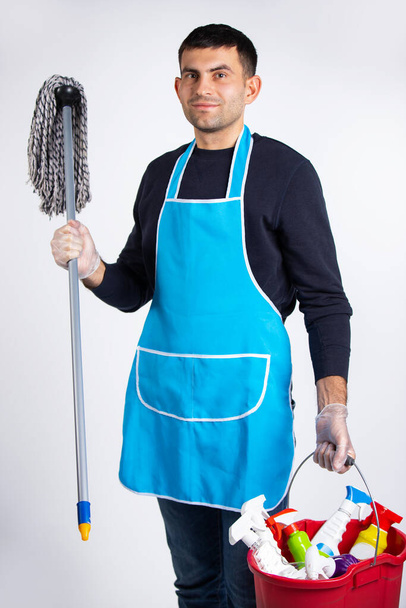 Gender stereotypes, a man in gloves, vabre and chemicals for cleaning the house. Photo on a white background. Cleaning and cleanliness concept. High quality photo - Foto, Bild