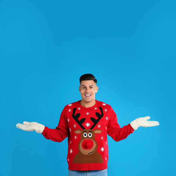 Happy man in Christmas sweater and mittens on blue background - Valokuva, kuva