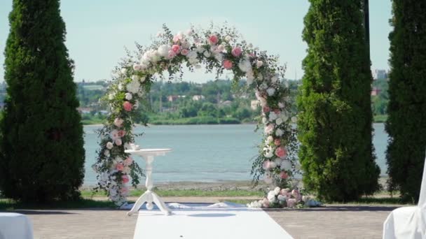Luogo per la cerimonia nuziale in colore bianco sullo sfondo del fiume. Arco nuziale con mazzi di rose pastello. Rallentatore. - Filmati, video