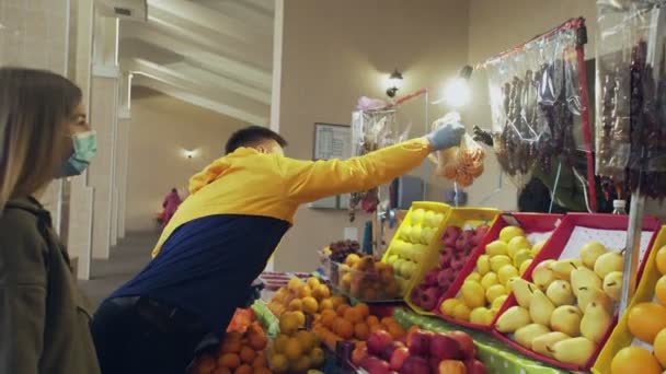 Mladý pár ochranných masek a rukavic si vybere dává provázkový sáček s ovocem k prodeji na trhu - Záběry, video