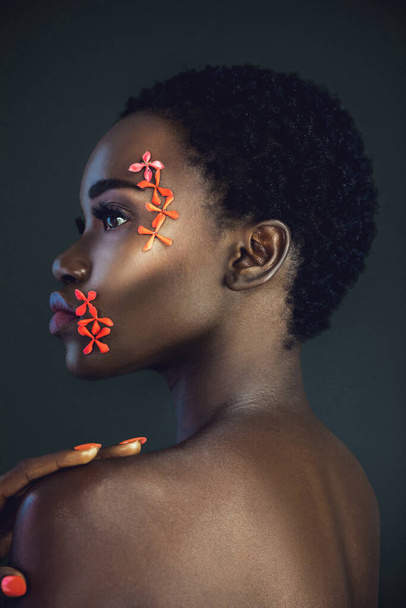 美しい短いアフロ、美しいメイク、紫色の唇とオレンジ色の爪を持つ官能的な若い黒人女性の肖像画彼女の顔にオレンジ色の花を身に着けている暗い背景を持つスタジオで自分自身によってポーズ. - 写真・画像