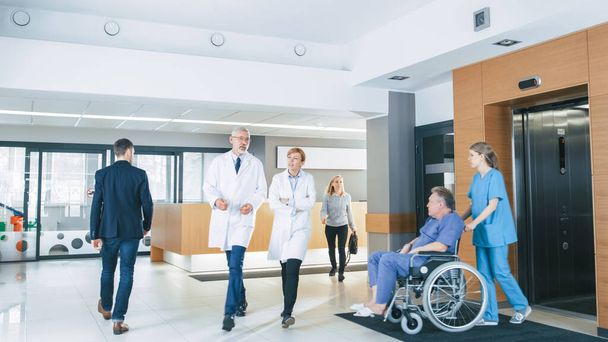 First Floor of the Busy Hospital, Doctors, Nurses and Personnel Busy Working, Assistant Moves Elderly Man in the Wheelchair. New Modern Medical Hospital with Professional Staff. - Valokuva, kuva