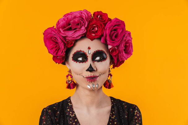 Pleased girl in halloween makeup and flower wreath posing at camera isolated over yellow wall - Фото, зображення