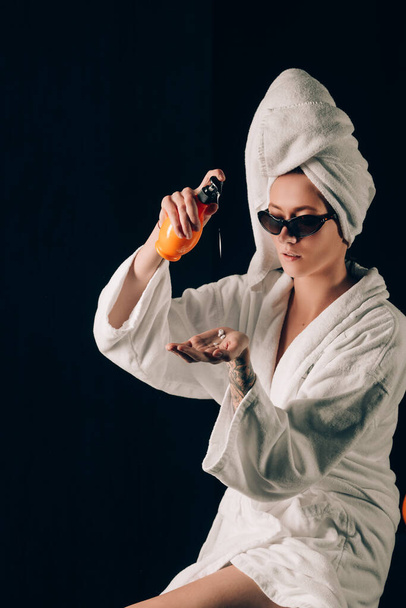 Soins de la peau, Femme dans les lunettes de soleil Appliquer la crème dans la serviette de bain après spa, Traitement cosmétique Lotion hydratante. Fond noir - Photo, image