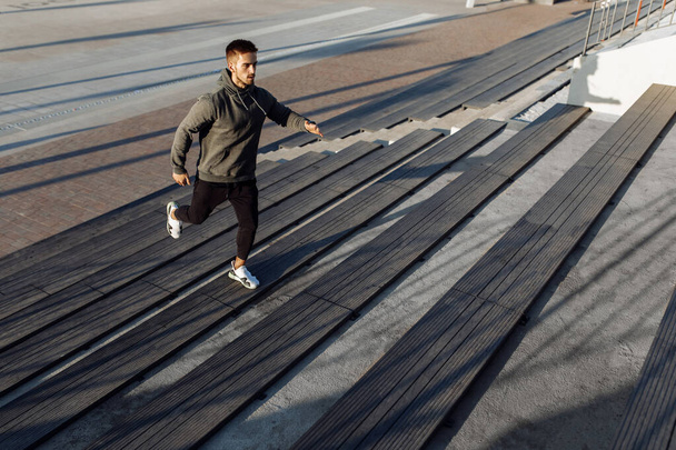 Спортивный молодой человек, в спортивной одежде, бег трусцой во время тренировок на открытом воздухе на городской лестнице, спорт, здоровый образ жизни - Фото, изображение