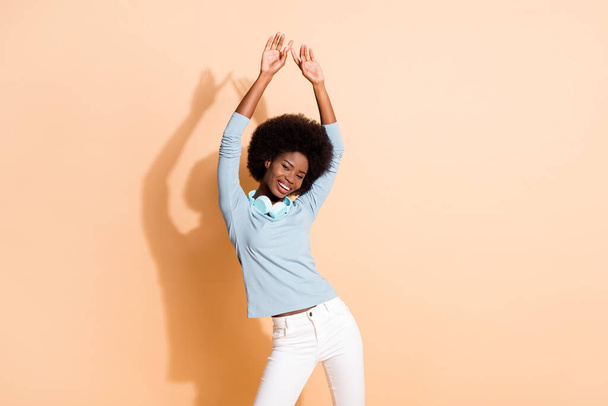 Photo portrait of african american woman dancing with both hands in air isolated on pastel beige colored background - Foto, Bild