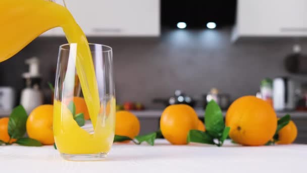 Jugo de naranja vertiendo en un vaso sobre una mesa blanca. Zumo cítrico salpicadura cámara lenta - Imágenes, Vídeo